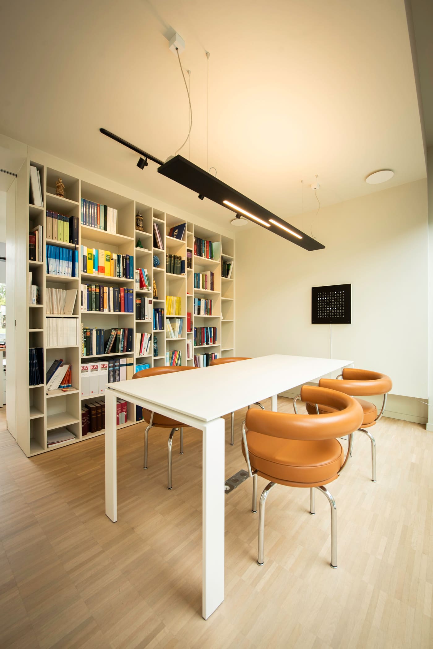 De bibliotheek van het kantoor met wetboeken, vergadertafel en cognackleurige stoelen