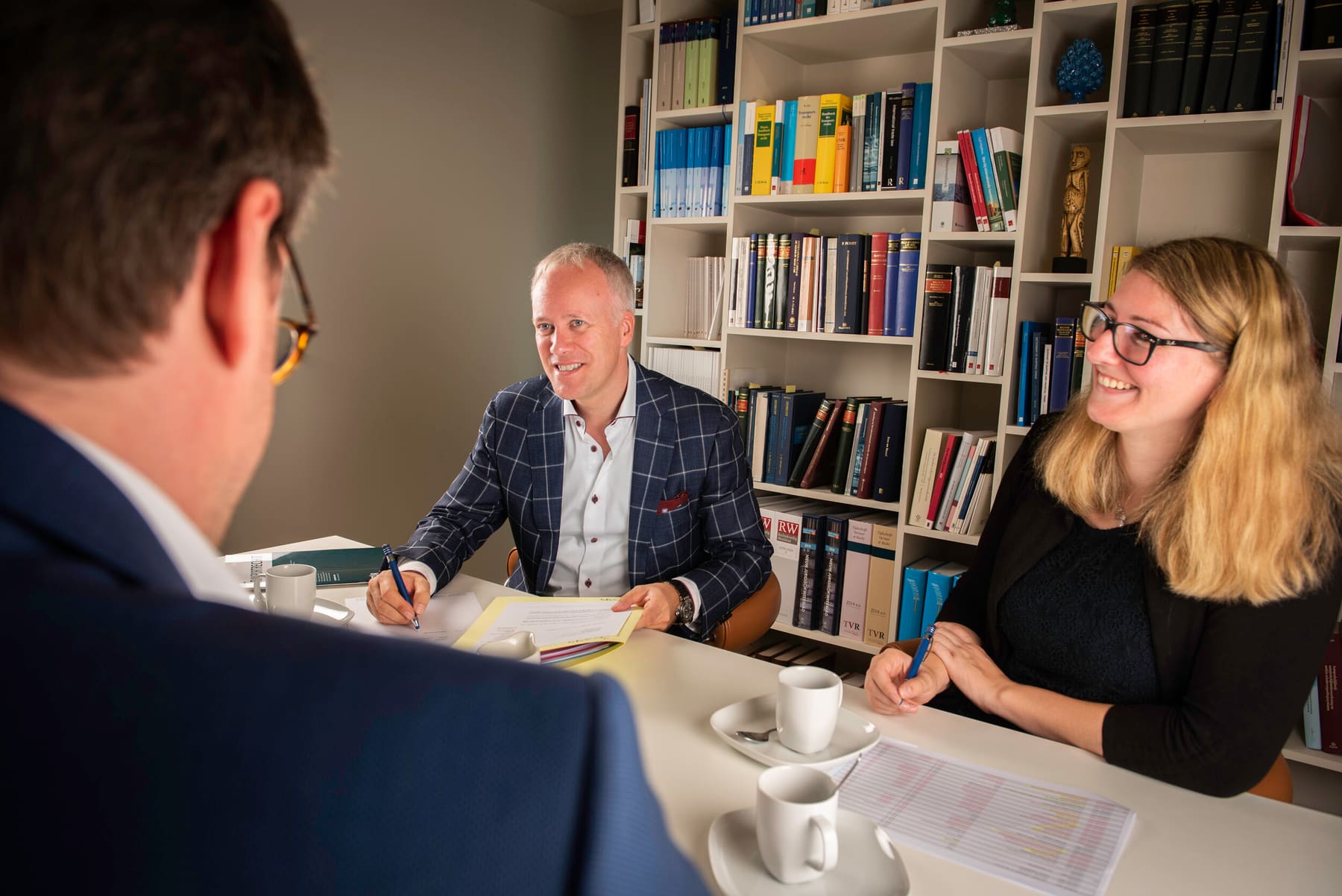 Filip Melis in overleg aan de vergadertafel van het kantoor, voor de wand met wetboeken